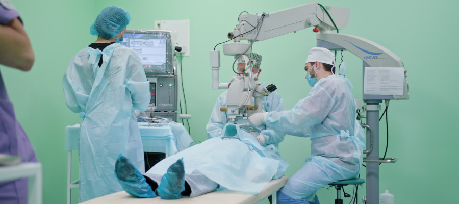Team of ophtalmology surgeons and assistants with ophtalomological surgery tools during surgical treatment. Two male surgeons operate the machinery. Camera comes closer. Indoor. Wide Angle. Stabilised